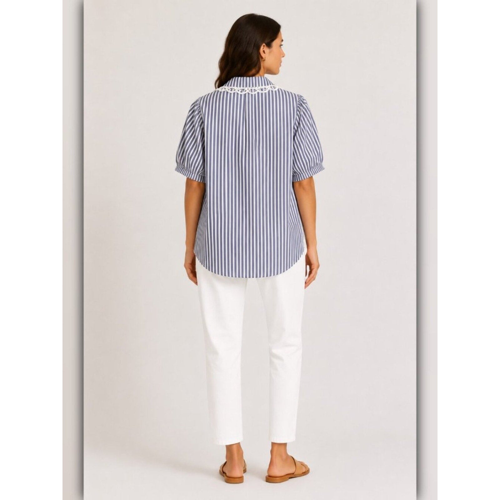 Woman wearing a blue and white striped shirt and white pants on a plain background