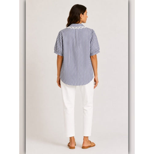 Woman wearing a blue and white striped shirt and white pants on a plain background