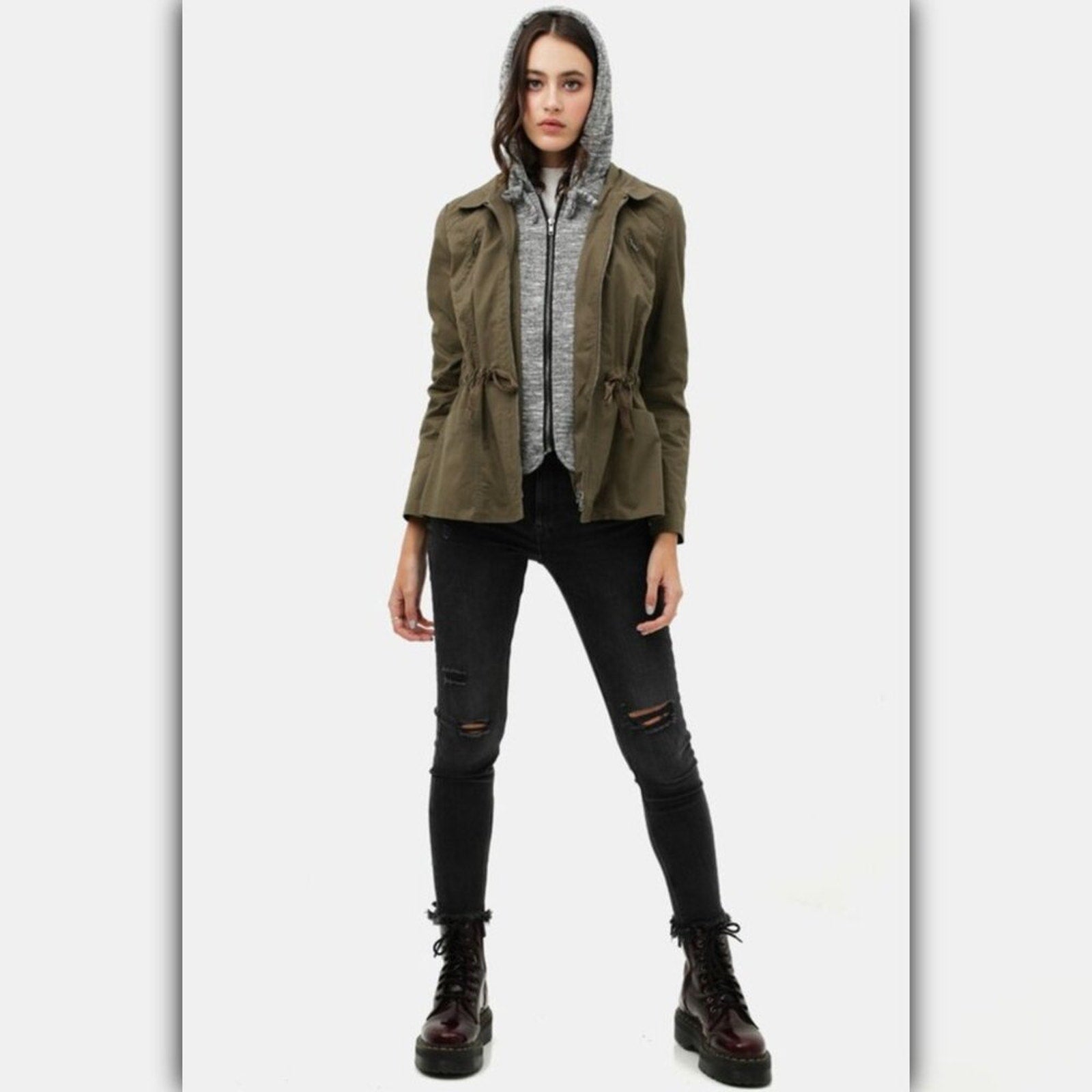 Person wearing a green jacket, black pants, and dark boots on a white background
