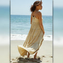 Woman in a beige dress standing on a beach with ocean in the background