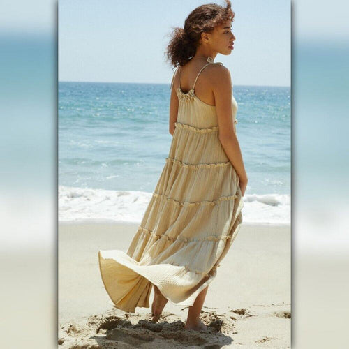 Woman in a beige dress standing on a beach with ocean in the background