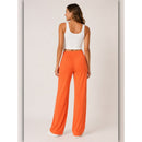 Woman wearing a white tank top and bright orange pants on a plain background