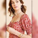 Woman wearing a red patterned blouse with jewelry on a beige background