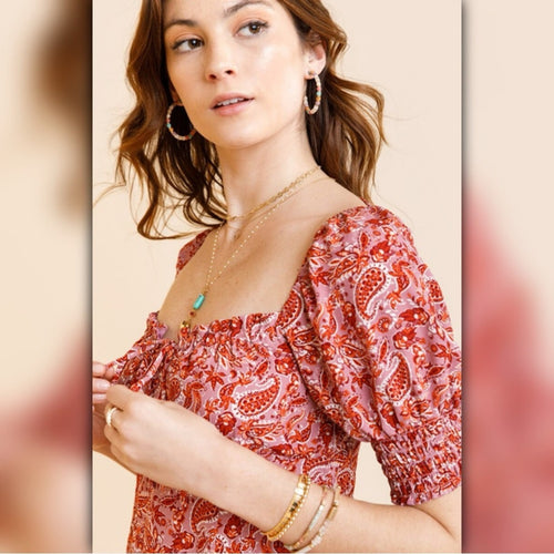 Woman wearing a red patterned blouse with jewelry on a beige background