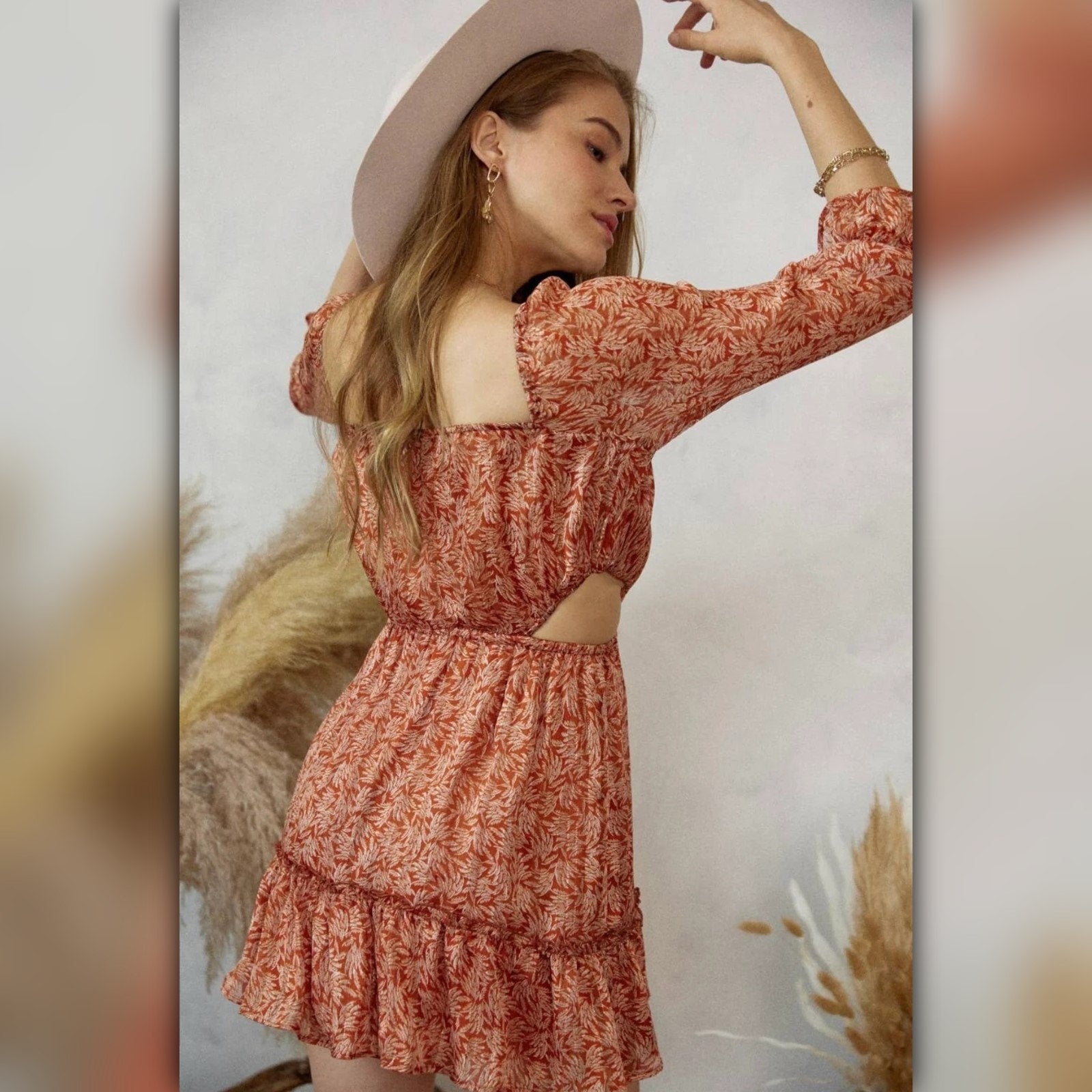 Woman wearing a floral dress with cut-out design and a wide-brimmed hat against a neutral background.