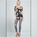 Woman wearing a floral top and ripped jeans on a plain background