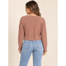 A woman shown from the back wearing a ribbed long-sleeve cropped sweater in a dusty rose color, paired with light blue jeans, against a solid beige background.
