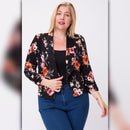 Plus size model wearing a black floral open front blazer with 3/4 sleeves, styled with a black top and blue jeans.