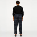 A model viewed from the back wearing navy blue windowpane plaid trousers and a black long-sleeve top, standing against a plain white studio background.