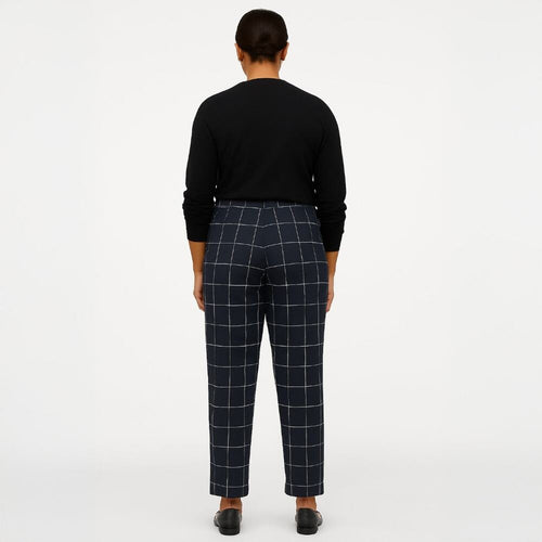 A model viewed from the back wearing navy blue windowpane plaid trousers and a black long-sleeve top, standing against a plain white studio background.