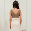 Woman wearing a brown tank top and white pants against a light gray background