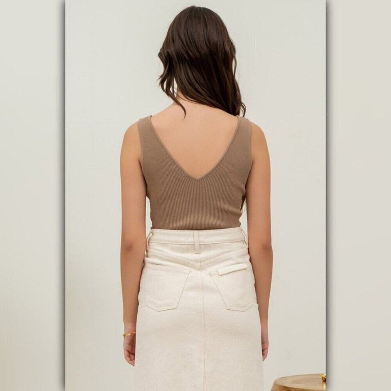 Woman wearing a brown tank top and white pants against a light gray background