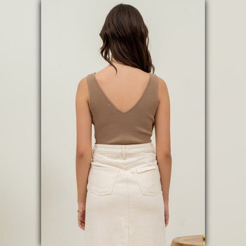 Woman wearing a brown tank top and white pants against a light gray background