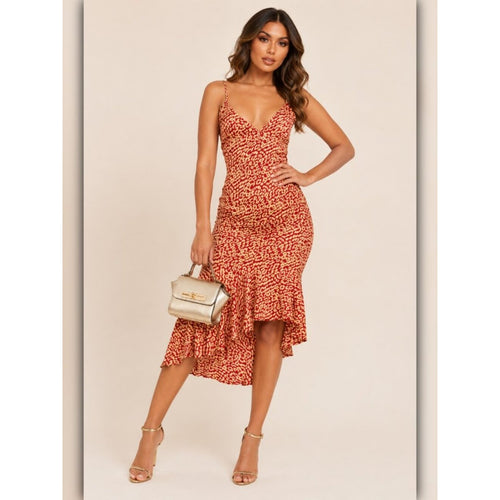 A woman models a red and orange abstract patterned midi dress with spaghetti straps and a ruffled hem, holding a small metallic handbag against a plain beige background.