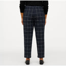 A person shown from the back wearing navy windowpane plaid trousers, a black long-sleeve top, and black shoes against a plain light gray studio background.
