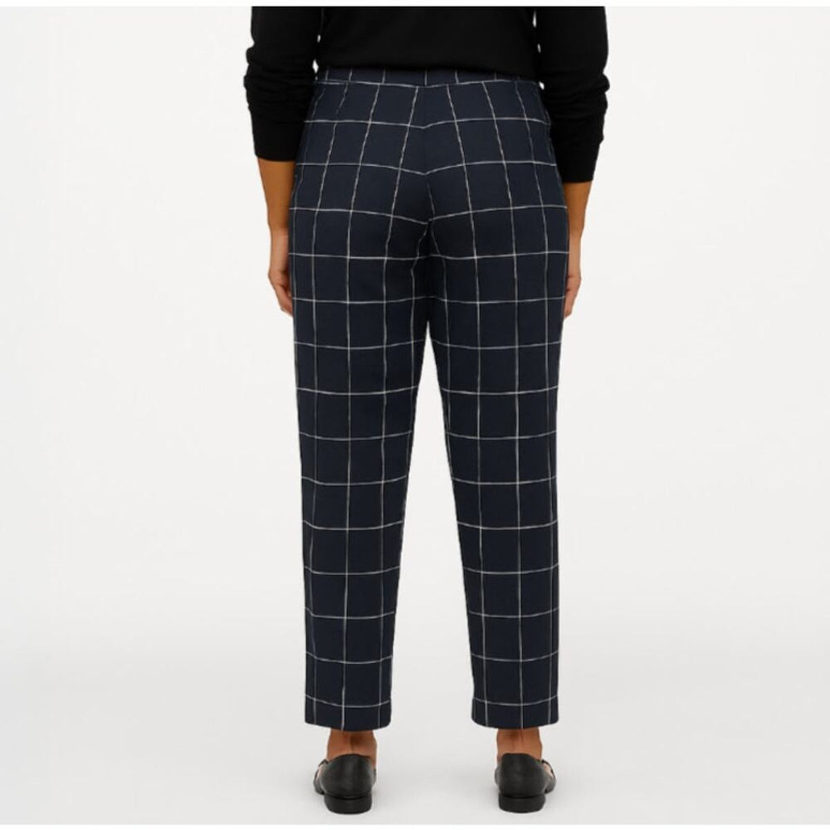 A person shown from the back wearing navy windowpane plaid trousers, a black long-sleeve top, and black shoes against a plain light gray studio background.