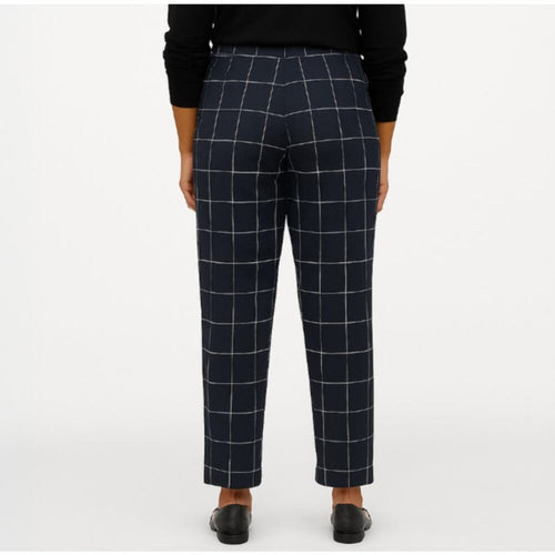 A person shown from the back wearing navy windowpane plaid trousers, a black long-sleeve top, and black shoes against a plain light gray studio background.