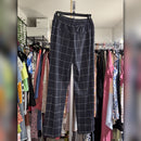 A pair of dark gray wide-leg trousers with a white windowpane grid pattern, hanging on a black hanger in a closet filled with clothing racks.