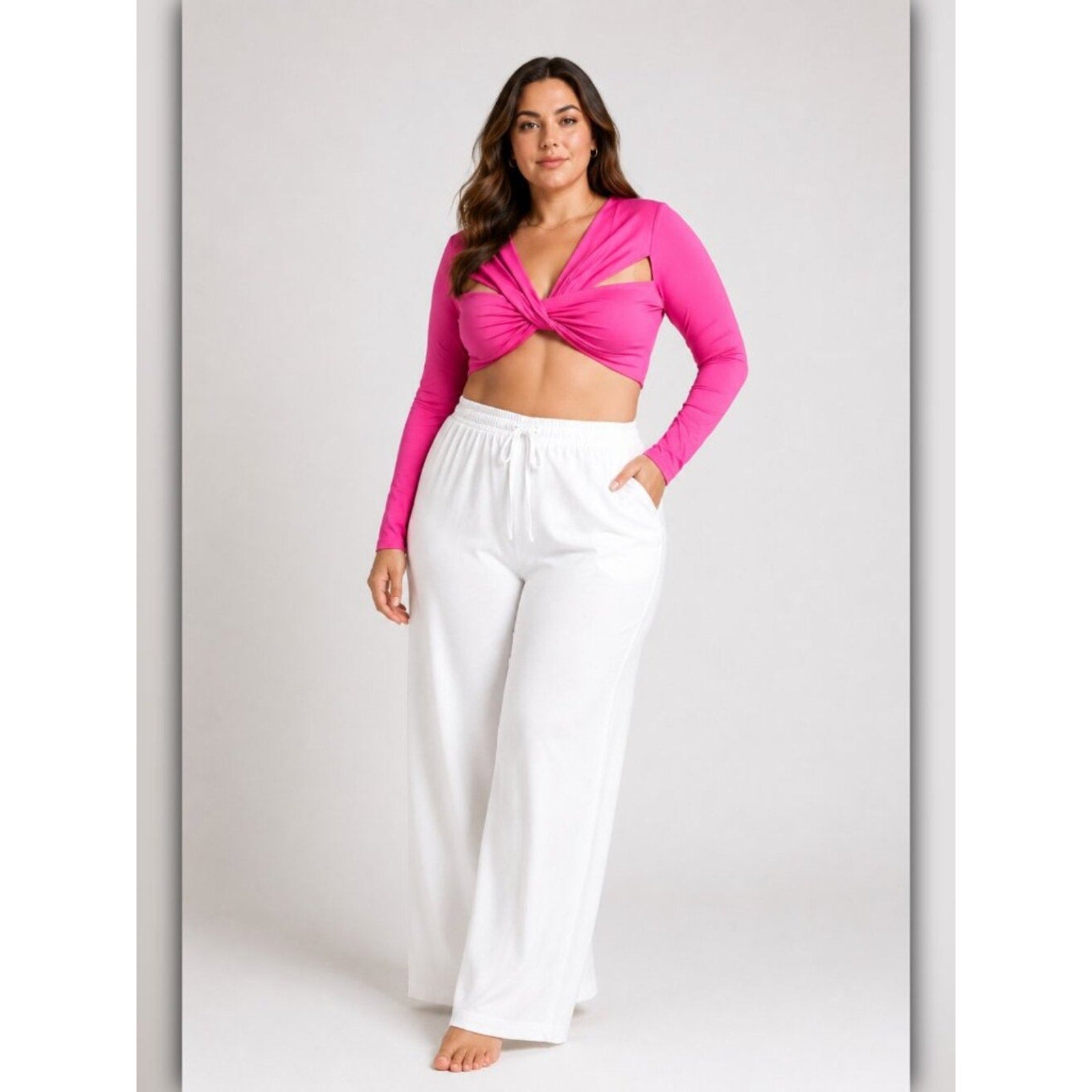 Woman wearing a bright pink long-sleeve top and white pants on a light gray background