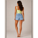 Woman wearing a light green top and denim shorts on a neutral background