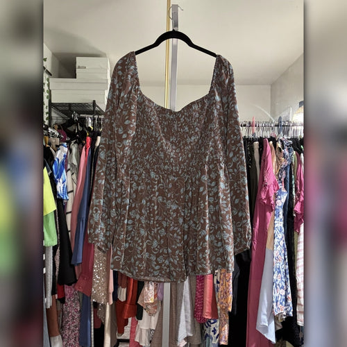 A brown long-sleeve top with a light floral pattern, hanging on a black hanger in a closet filled with other clothes.