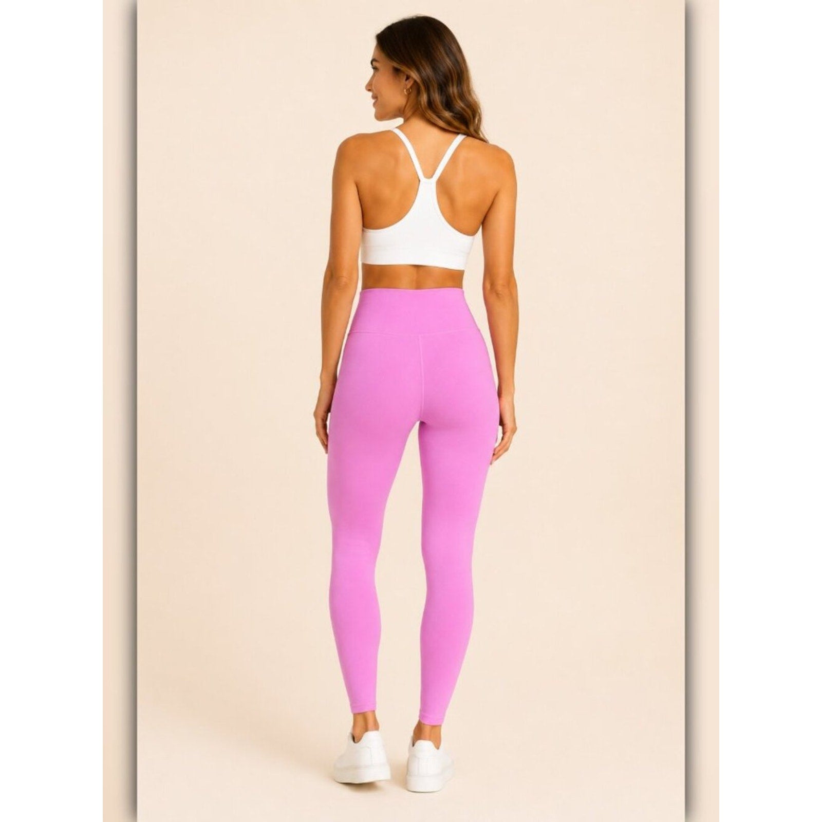 Woman wearing pink leggings and a white sports bra on a beige background