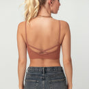 Woman wearing a brown strappy top and blue jeans on a light gray background