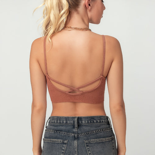 Woman wearing a brown strappy top and blue jeans on a light gray background