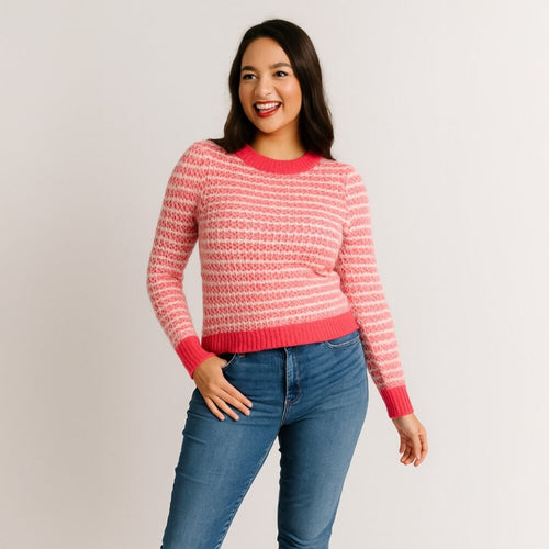 Woman wearing a pink and white patterned sweater with blue jeans on a plain background