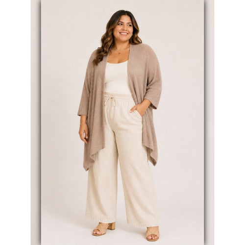 A woman modeling a light taupe open-front knit cardigan over a white tank top and cream wide-leg drawstring pants, standing against a light beige studio background.